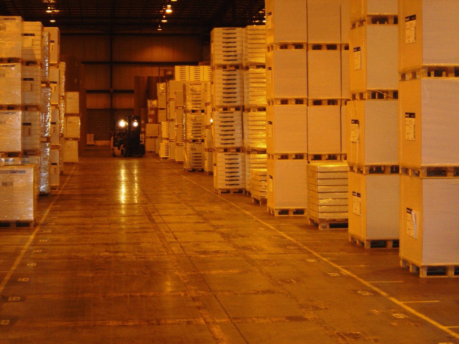 Palletized goods in a warehouse aisle with a forklift at work.